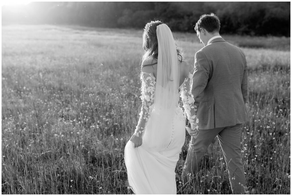 Black and white image of bride and groom walking through field at Cripps Barn wedding
