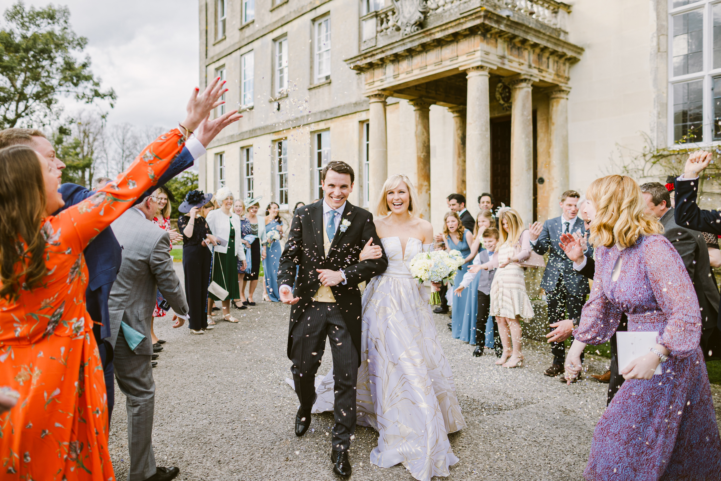 Bride and groom walking through confetti outside Elmore Court, photographed by a recommended Elmore Court wedding photographer.
