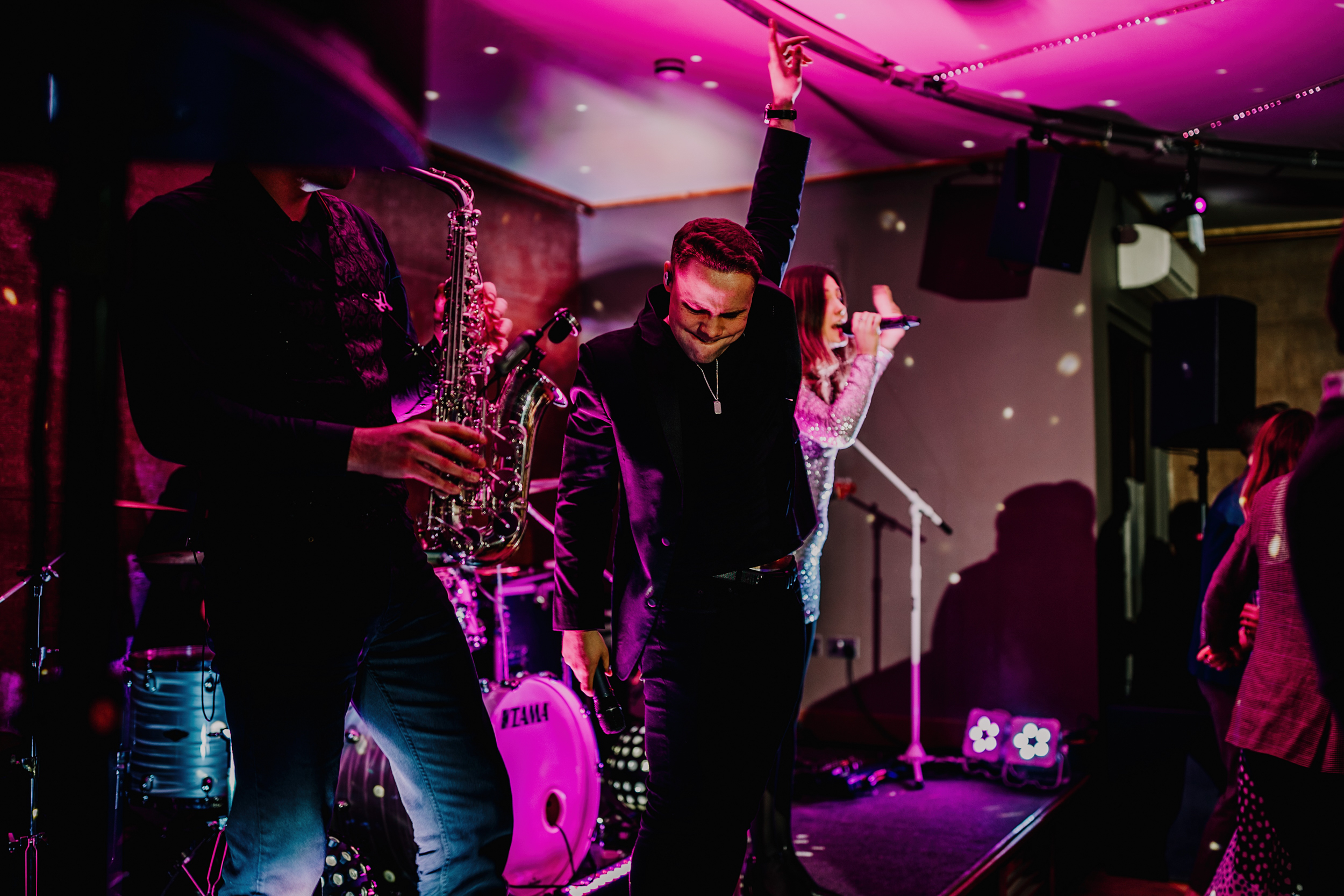 lead singer of band in the gillyflower with his hand in the air, lit with purple light and in the middle of a song