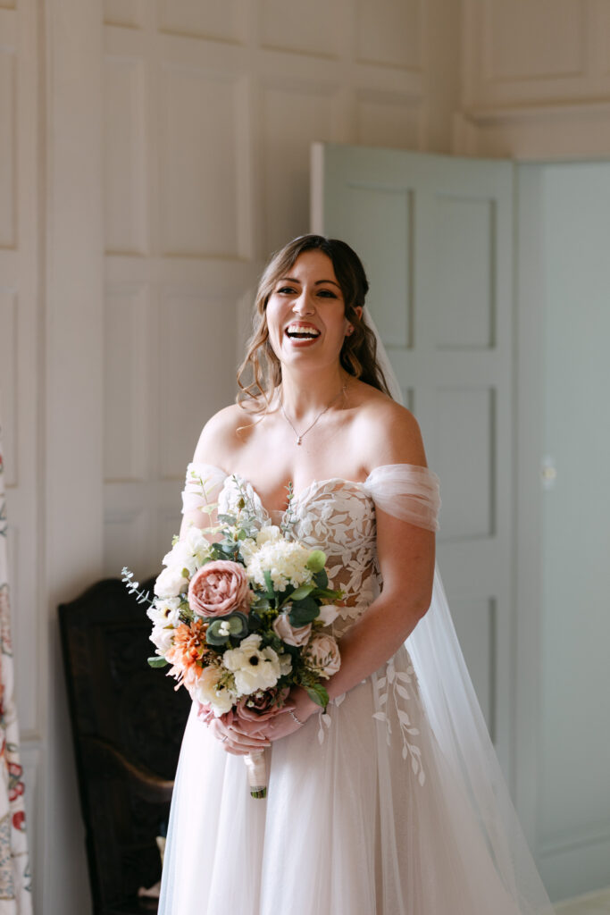 Natural bridal portrait at Elmore Court, bride laughing while holding bouquet in soft window light