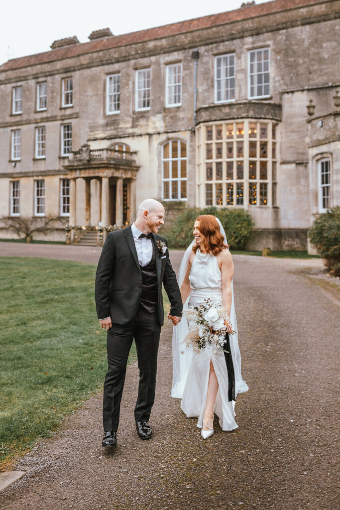 Winter wedding couple portrait outside Elmore Court, walking together in front of the main house