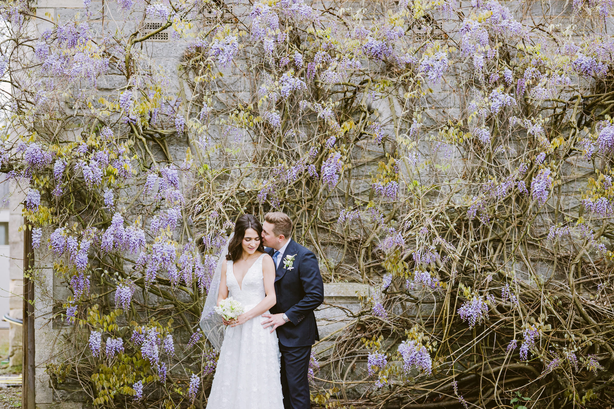Couple standing together beneath wisteria in the gardens at Elmore Court during spring wedding portraits