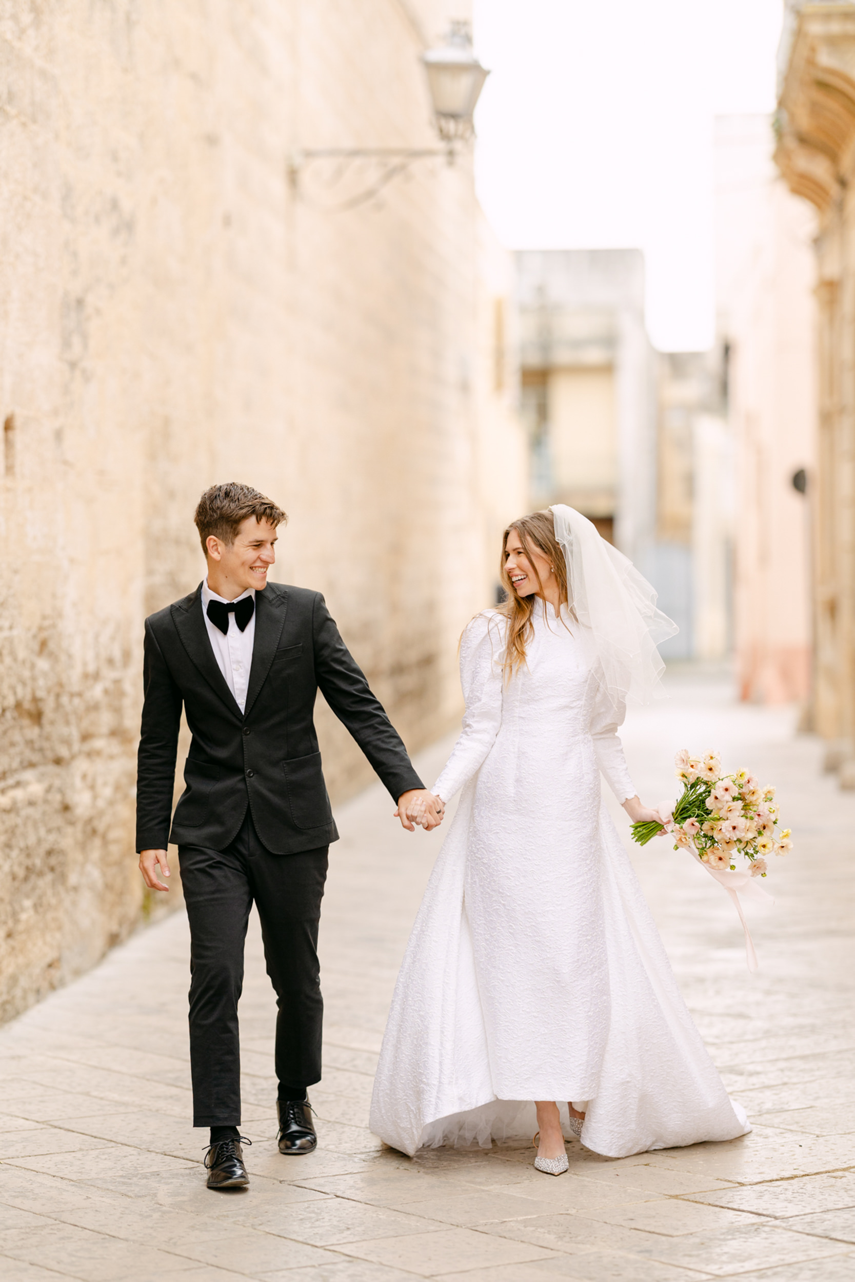 bride and groom walking and laughing walking down an old Italian town street in Puglia