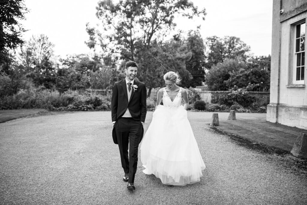 Bride and groom walking together outside Elmore Court, laughing as they stroll across the gravel driveway.