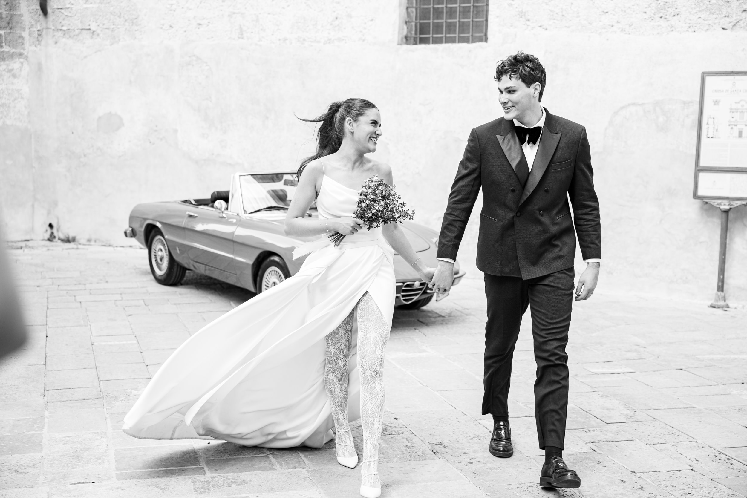 bride and groom holding hands and walking away and looking at each other in an old Italian town