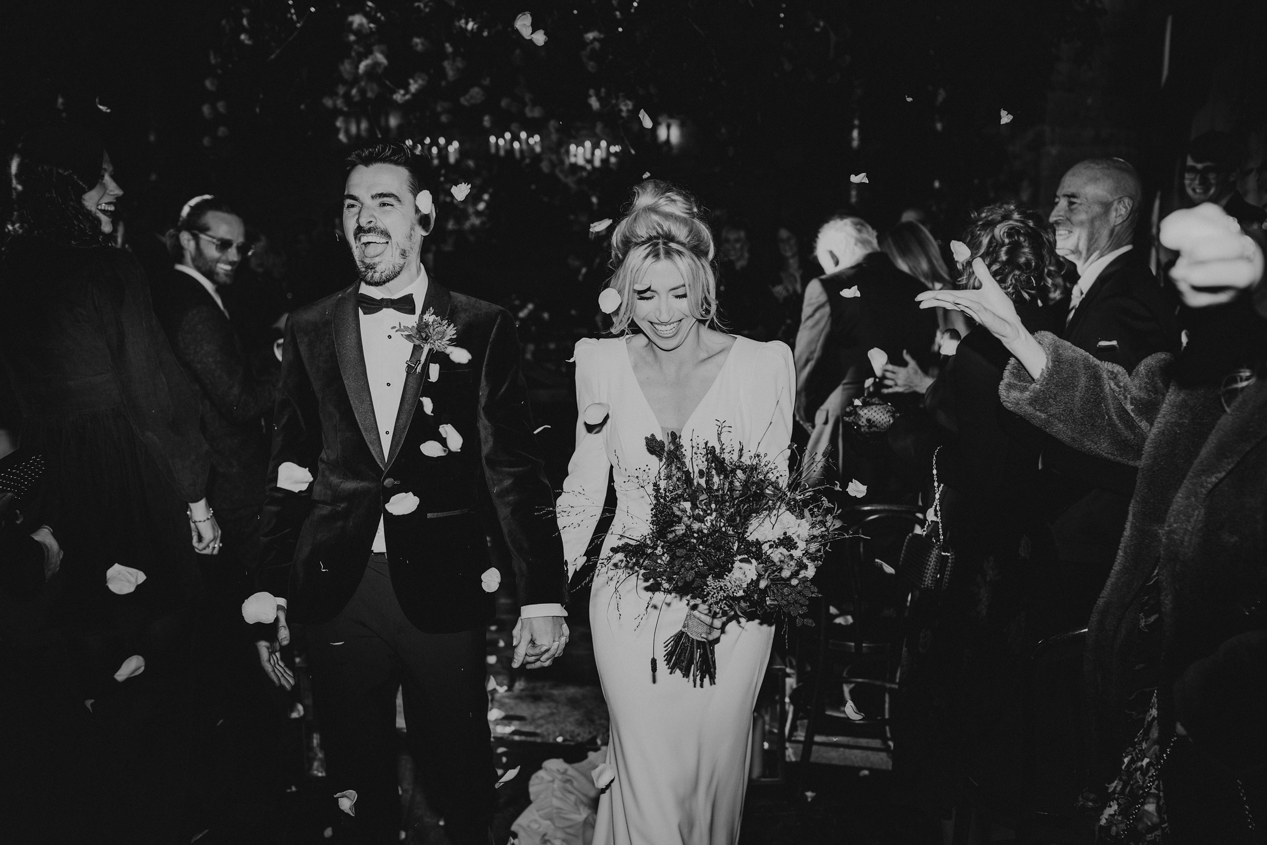 editorial black and white of couple holding hands inside Cripps Barn, walking through confetti